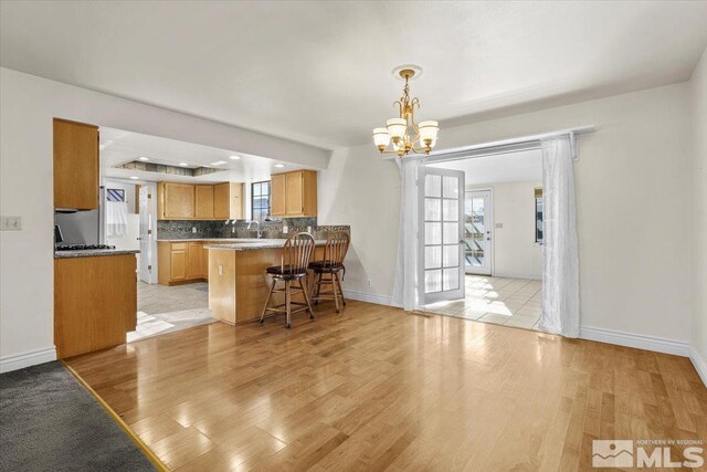 kitchen with light hardwood / wood-style flooring, a kitchen breakfast bar, decorative backsplash, decorative light fixtures, and kitchen peninsula
