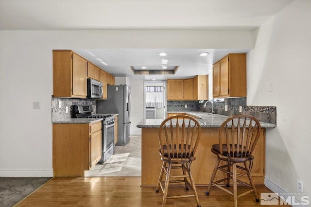 kitchen featuring a breakfast bar area, stainless steel appliances, kitchen peninsula, decorative backsplash, and a raised ceiling
