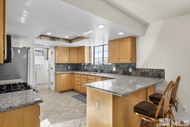kitchen with kitchen peninsula, sink, a kitchen breakfast bar, decorative backsplash, and a tray ceiling