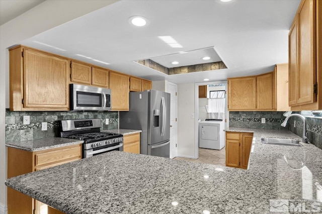 kitchen featuring a tray ceiling, washer / dryer, sink, kitchen peninsula, and stainless steel appliances