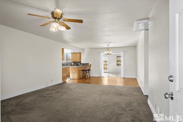 unfurnished living room with ceiling fan with notable chandelier and dark colored carpet