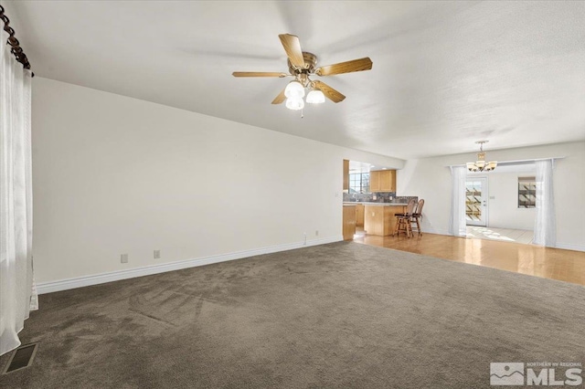 unfurnished living room featuring ceiling fan with notable chandelier and dark colored carpet