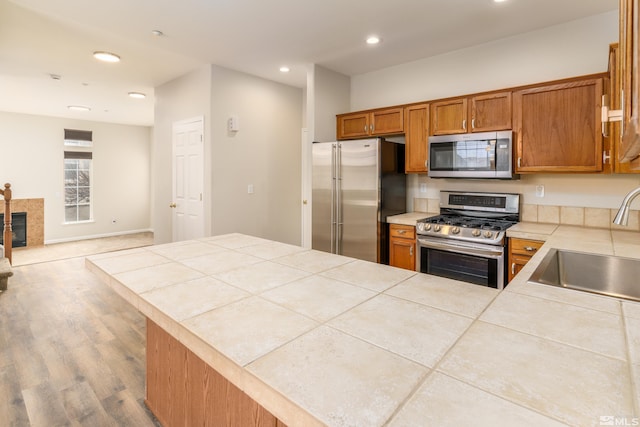 kitchen with sink, stainless steel appliances, wood-type flooring, a tiled fireplace, and tile countertops