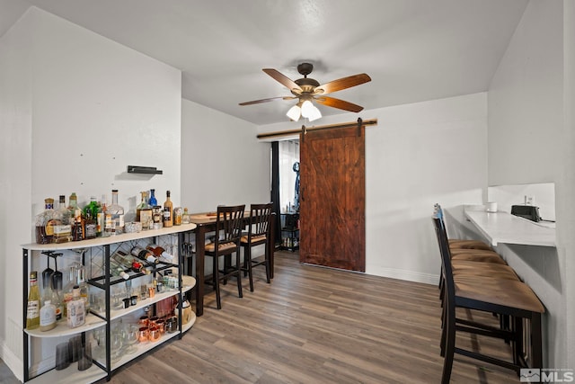 dining space featuring a barn door, baseboards, ceiling fan, wood finished floors, and a bar