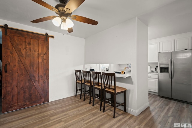 kitchen featuring stainless steel fridge, a breakfast bar, wood finished floors, and a barn door