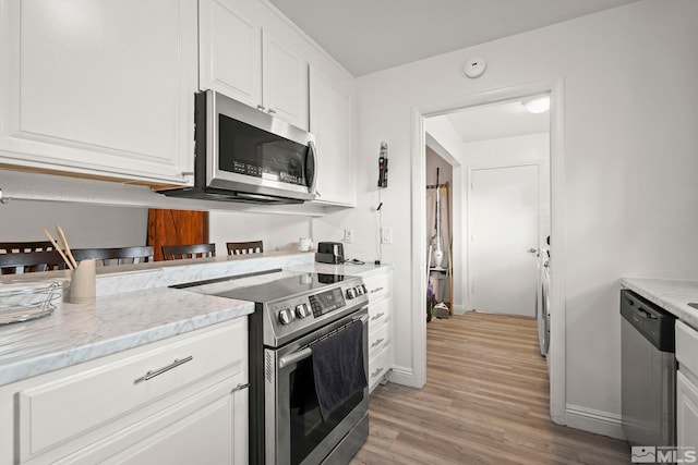 kitchen with light wood-style flooring, white cabinetry, stainless steel appliances, and light stone counters