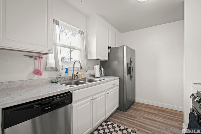 kitchen with stainless steel appliances, light wood-style flooring, white cabinetry, a sink, and baseboards