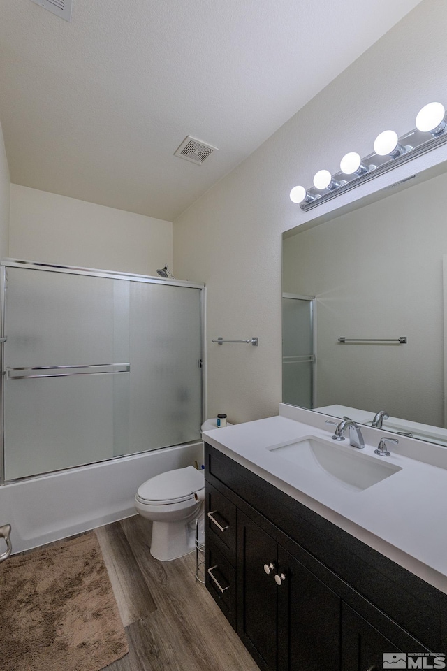 full bathroom featuring hardwood / wood-style flooring, vanity, combined bath / shower with glass door, and toilet