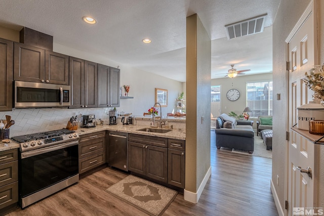 kitchen with sink, light stone counters, dark brown cabinets, light hardwood / wood-style flooring, and appliances with stainless steel finishes