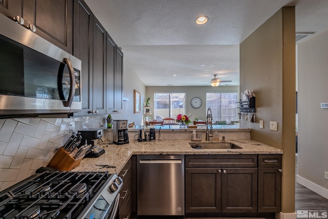 kitchen with dark brown cabinetry, stainless steel appliances, light stone countertops, and sink