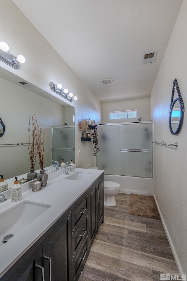 full bathroom featuring bath / shower combo with glass door, hardwood / wood-style floors, vanity, and toilet