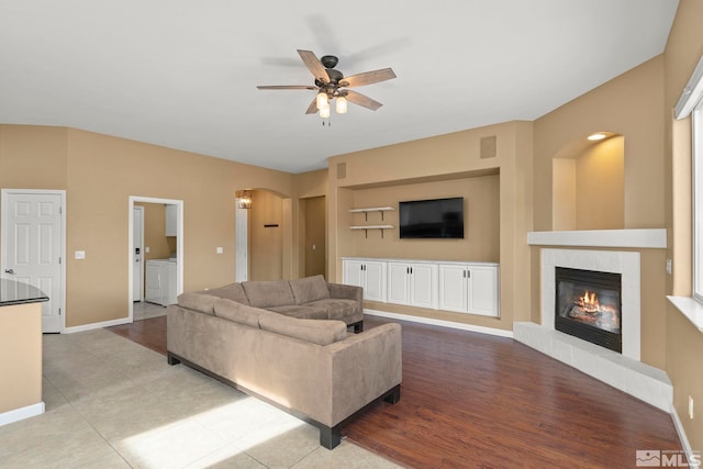 living room with a tiled fireplace, light hardwood / wood-style flooring, washer and dryer, and ceiling fan