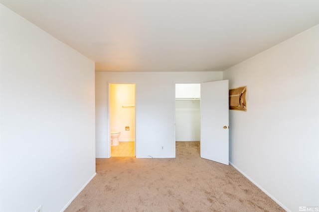 unfurnished bedroom with a spacious closet, light colored carpet, ensuite bath, and a closet