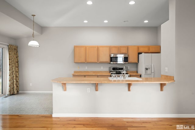 kitchen featuring a kitchen bar, decorative light fixtures, light wood-type flooring, and appliances with stainless steel finishes