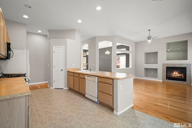 kitchen featuring sink, a tile fireplace, ceiling fan, white dishwasher, and light hardwood / wood-style floors