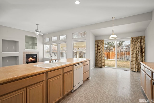 kitchen with sink, a tiled fireplace, hanging light fixtures, ceiling fan, and white dishwasher