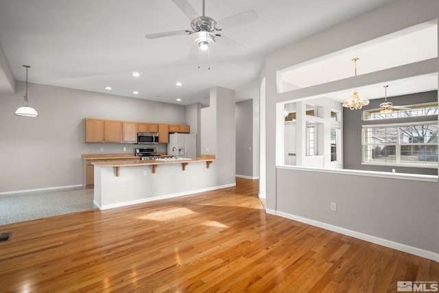 kitchen featuring pendant lighting, a kitchen bar, kitchen peninsula, stainless steel appliances, and light hardwood / wood-style flooring