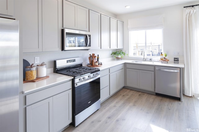 kitchen with sink, light hardwood / wood-style flooring, gray cabinets, and appliances with stainless steel finishes