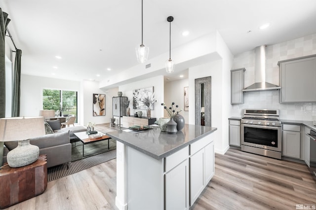 kitchen featuring gas range, gray cabinets, hanging light fixtures, and wall chimney range hood