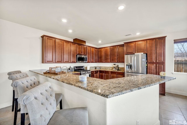 kitchen featuring a breakfast bar area, light tile patterned floors, light stone counters, kitchen peninsula, and stainless steel appliances