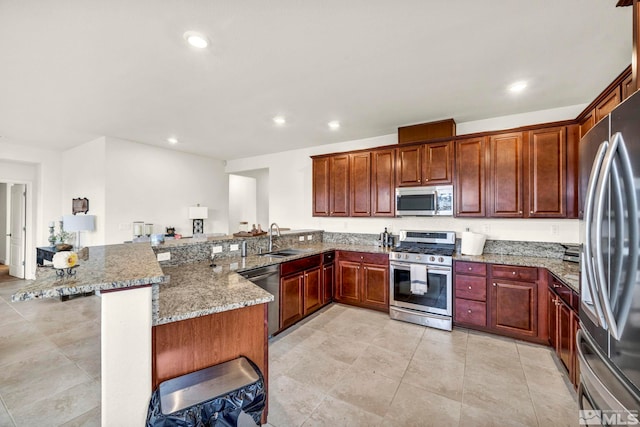 kitchen with sink, a breakfast bar, appliances with stainless steel finishes, light stone counters, and kitchen peninsula