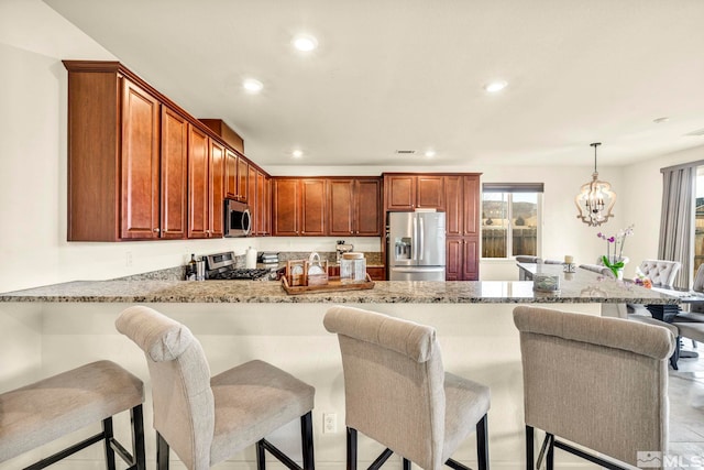 kitchen featuring appliances with stainless steel finishes, a kitchen breakfast bar, light stone counters, decorative light fixtures, and kitchen peninsula