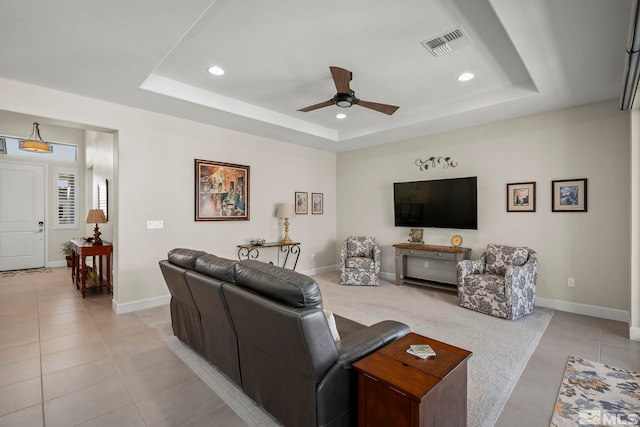 living room featuring a raised ceiling, light tile patterned floors, and ceiling fan