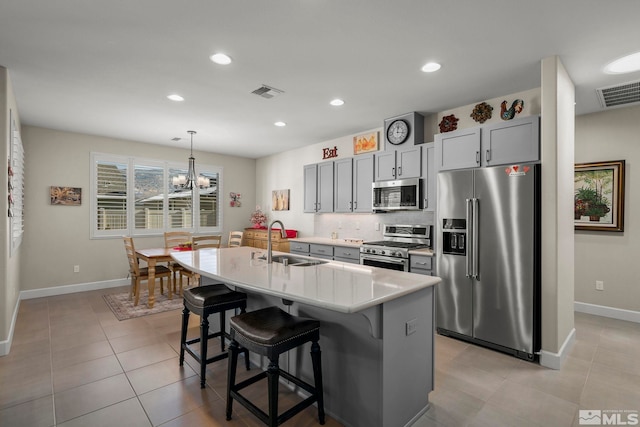 kitchen with sink, gray cabinets, a breakfast bar, appliances with stainless steel finishes, and a kitchen island with sink