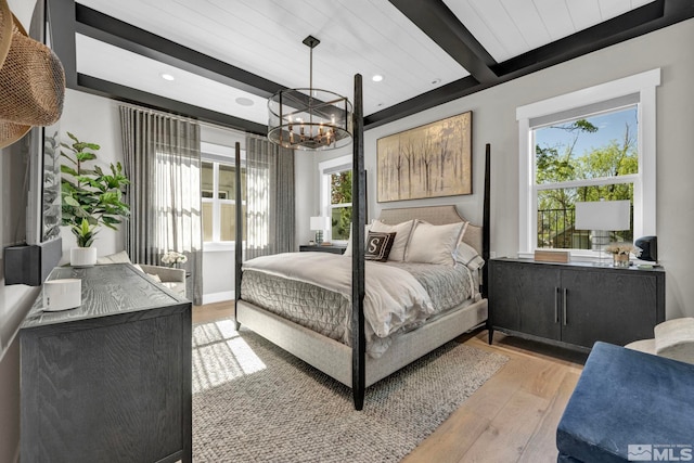 bedroom featuring multiple windows, a chandelier, beamed ceiling, and light wood-type flooring