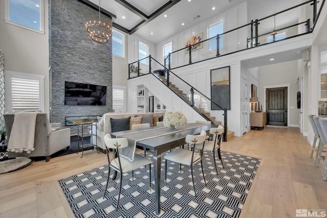 living room featuring a notable chandelier, a towering ceiling, light hardwood / wood-style floors, and beamed ceiling