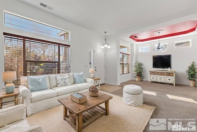 living room featuring a raised ceiling, a towering ceiling, light carpet, and a notable chandelier