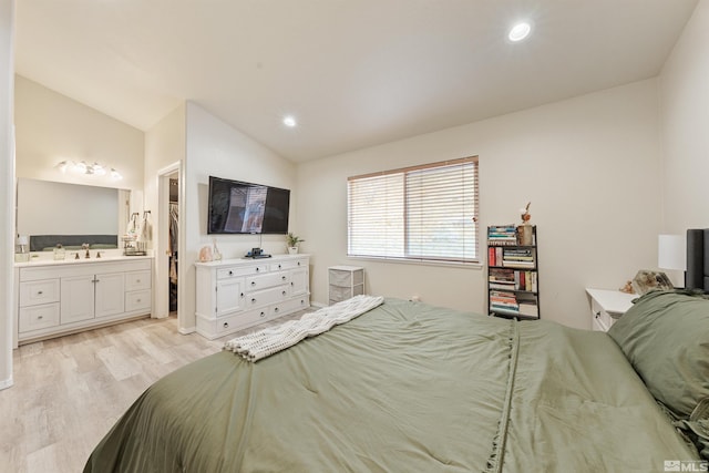 bedroom featuring sink, ensuite bath, vaulted ceiling, and light wood-type flooring