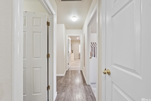 corridor with a textured ceiling and light wood-type flooring