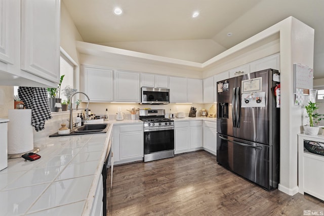 kitchen featuring sink, appliances with stainless steel finishes, white cabinetry, tile counters, and vaulted ceiling