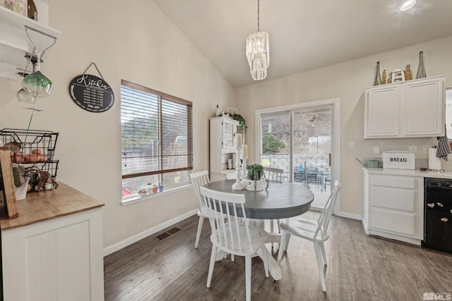 dining room featuring hardwood / wood-style flooring, vaulted ceiling, a wealth of natural light, and an inviting chandelier