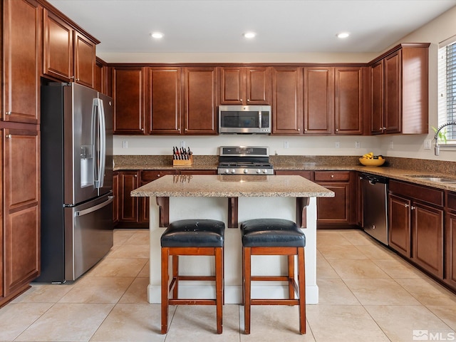 kitchen with sink, light tile patterned floors, a breakfast bar, appliances with stainless steel finishes, and a center island