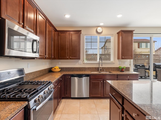 kitchen featuring stainless steel appliances, sink, light tile patterned floors, and dark stone counters