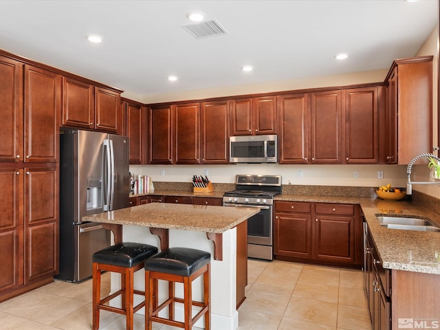 kitchen with sink, a kitchen breakfast bar, stainless steel appliances, a center island, and light stone countertops