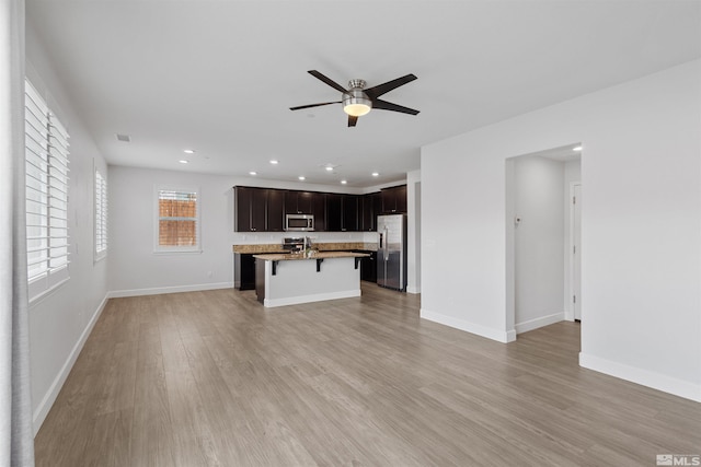 kitchen with a kitchen bar, ceiling fan, stainless steel appliances, a center island with sink, and light hardwood / wood-style flooring