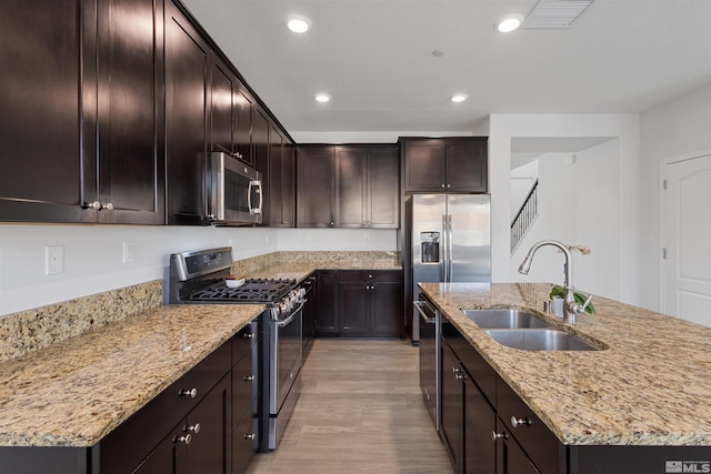 kitchen with sink, light stone counters, a center island with sink, stainless steel appliances, and light hardwood / wood-style floors