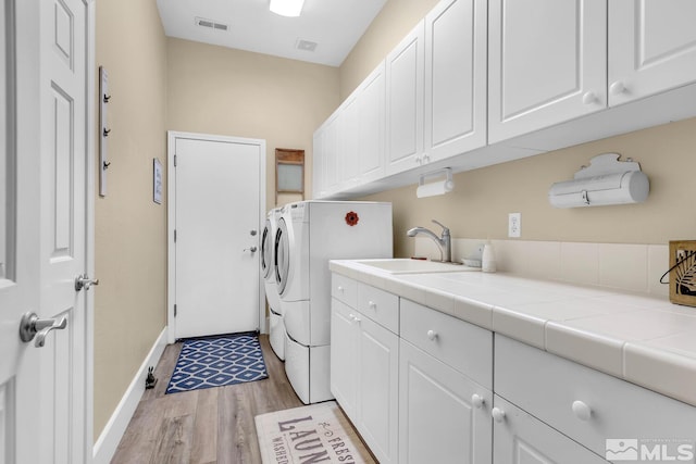 laundry area featuring cabinets, washer and clothes dryer, sink, and light wood-type flooring