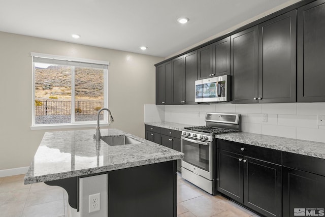 kitchen featuring stainless steel appliances, sink, a kitchen island with sink, and light stone counters