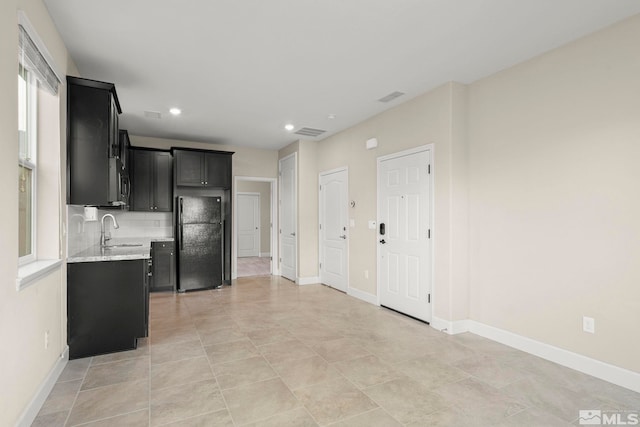 kitchen featuring black refrigerator, sink, decorative backsplash, and light stone countertops