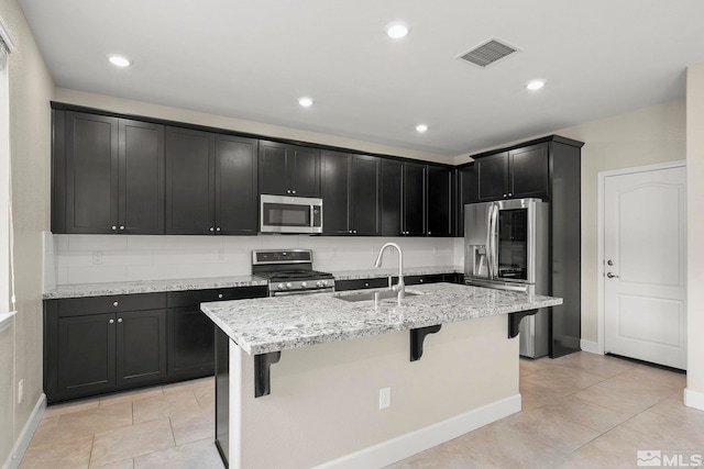 kitchen with sink, a kitchen bar, stainless steel appliances, light stone counters, and a center island with sink