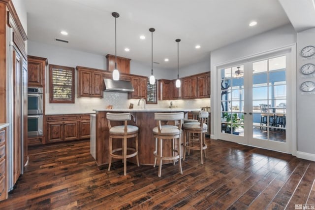 kitchen featuring tasteful backsplash, a center island, ventilation hood, hanging light fixtures, and dark hardwood / wood-style flooring