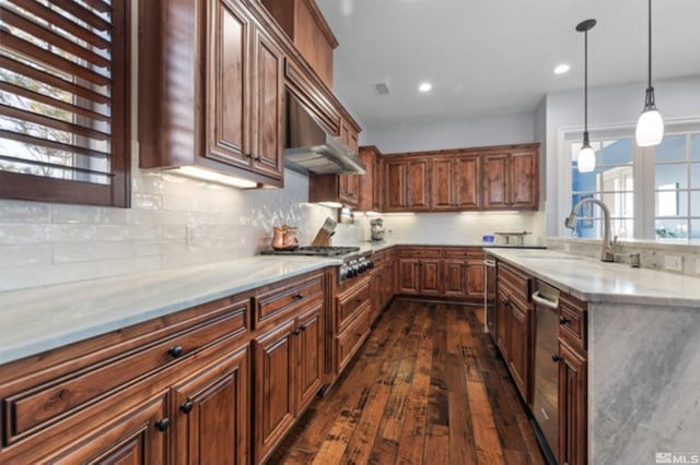 kitchen featuring wall chimney exhaust hood, sink, hanging light fixtures, appliances with stainless steel finishes, and light stone countertops