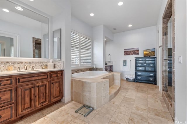 bathroom with a relaxing tiled tub, vanity, and decorative backsplash