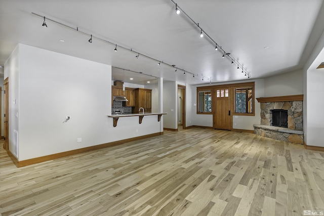 unfurnished living room with rail lighting, a stone fireplace, sink, and light wood-type flooring