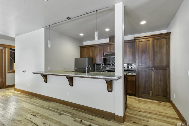 kitchen featuring light stone countertops, a breakfast bar, stainless steel refrigerator, and light hardwood / wood-style floors