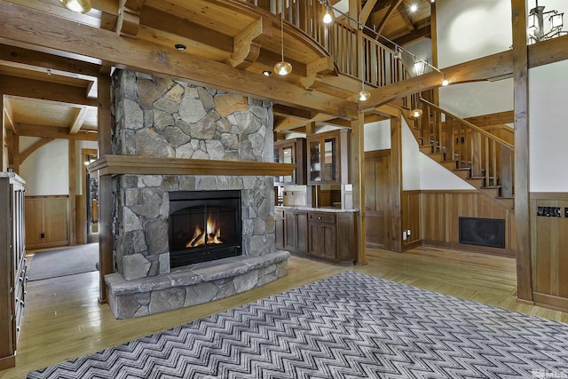 living room with a stone fireplace, wood walls, wood-type flooring, vaulted ceiling with beams, and wood ceiling